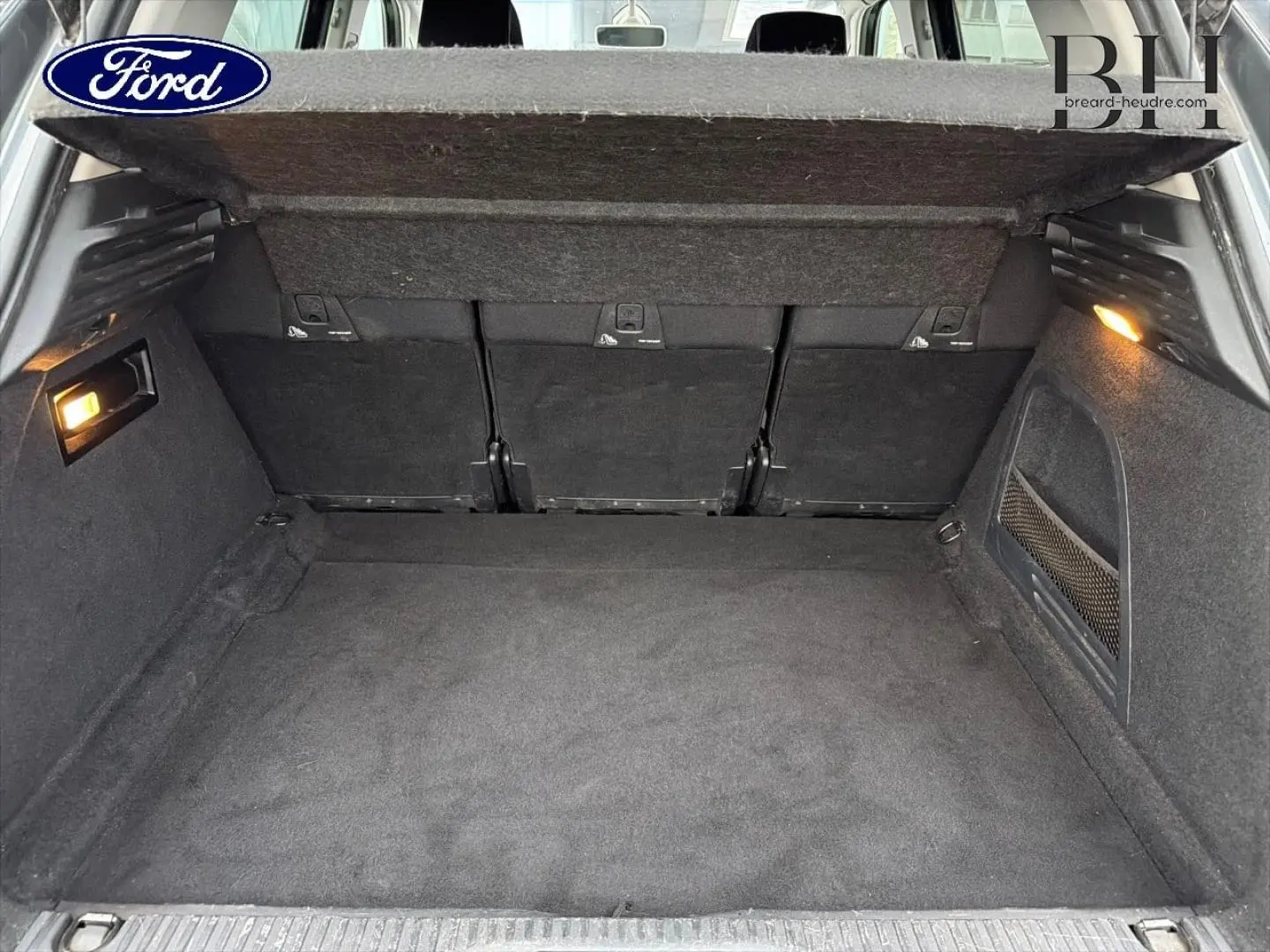 Coffre ouvert vu de l'arrière d'un Citroën C4 Picasso gris Shark avec habillage intérieur noir et éclairage latéral.
