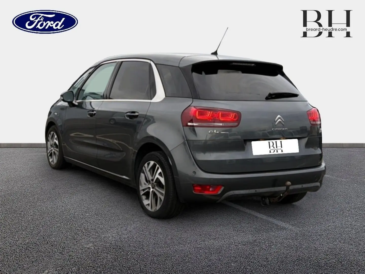 Citroën C4 Picasso gris Shark vue 3/4 arrière droit avec feux allumés et attelage visible.