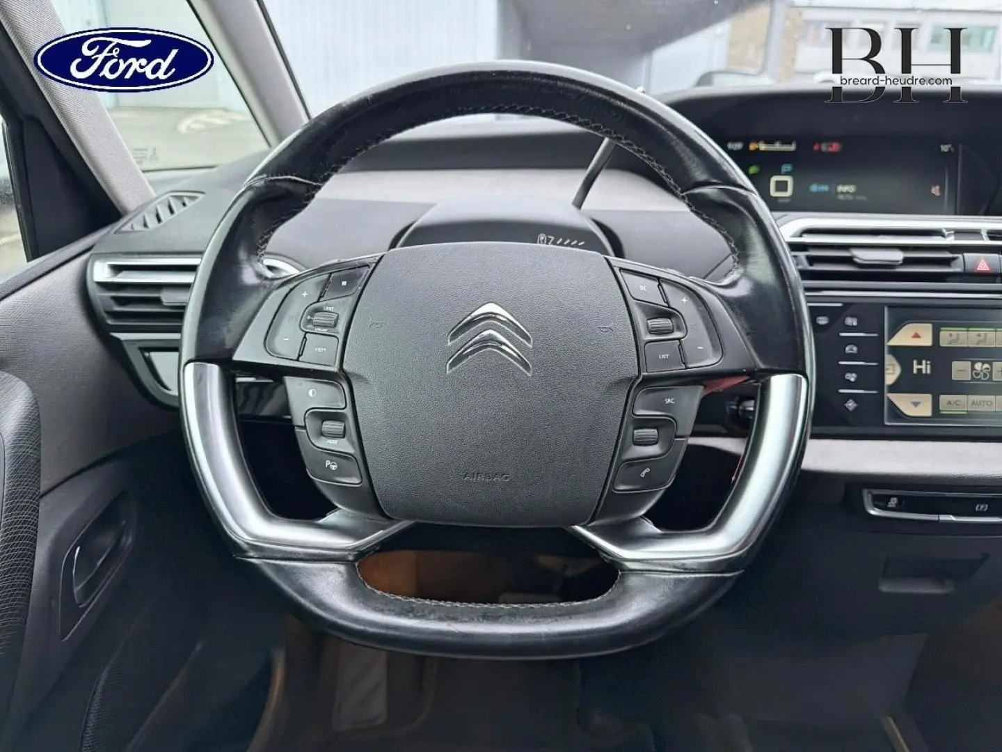 Gros plan sur le volant cuir multifonction Citroën C4 Picasso gris, avec tableau de bord et écran tactile en arrière-plan.