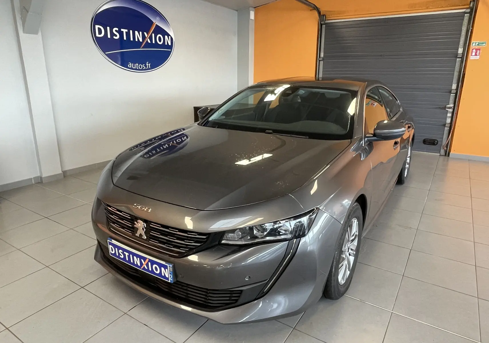 Peugeot 508 gris platinium vue 3/4 avant droit dans un showroom avec logo Distinxion en arrière-plan.