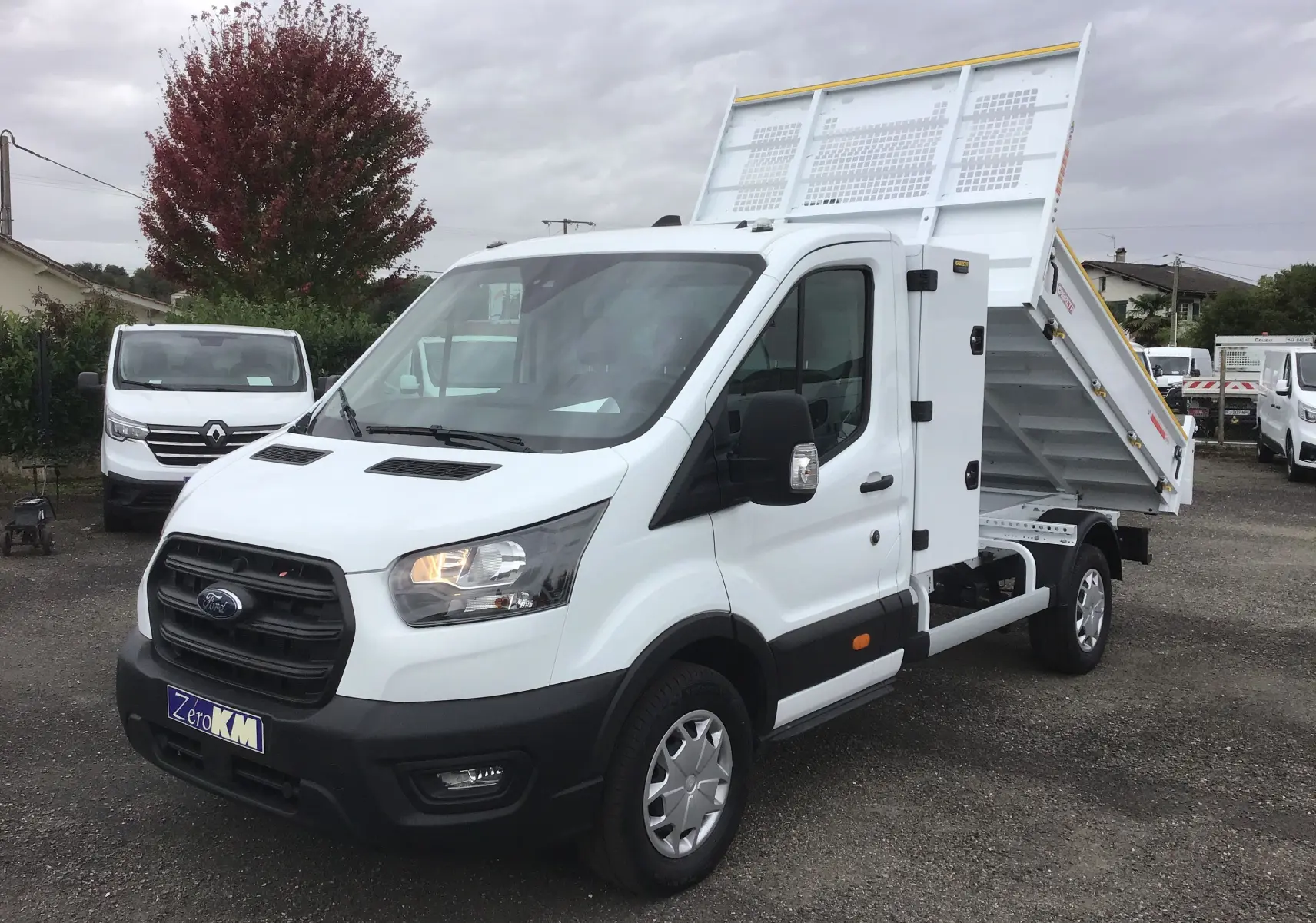 Ford Transit Chassis cabine blanc en 3/4 avant droit avec benne relevée et coffre latéral visible.