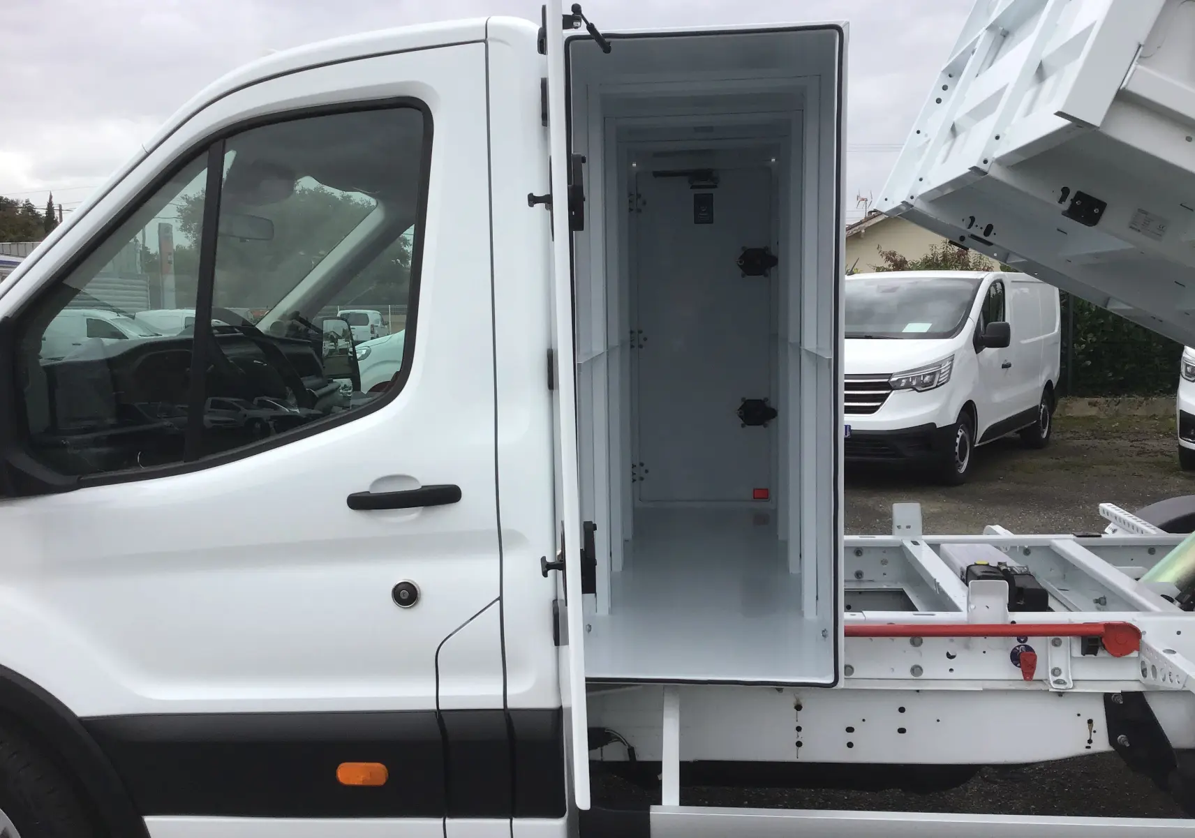 Vue latérale gauche d'un Ford Transit blanc avec benne relevée et coffre ouvert sur châssis cabine.