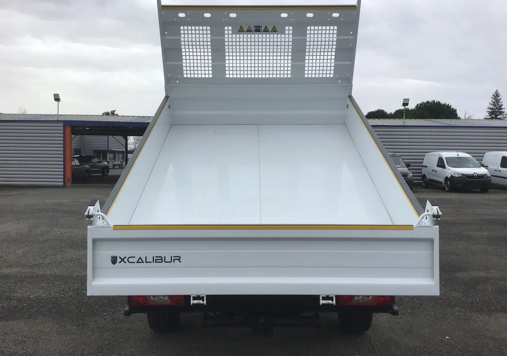 Vue arrière frontale d'une benne blanche Xcalibur sur un Ford Transit Chassis Cabine 2024, plateau relevé.