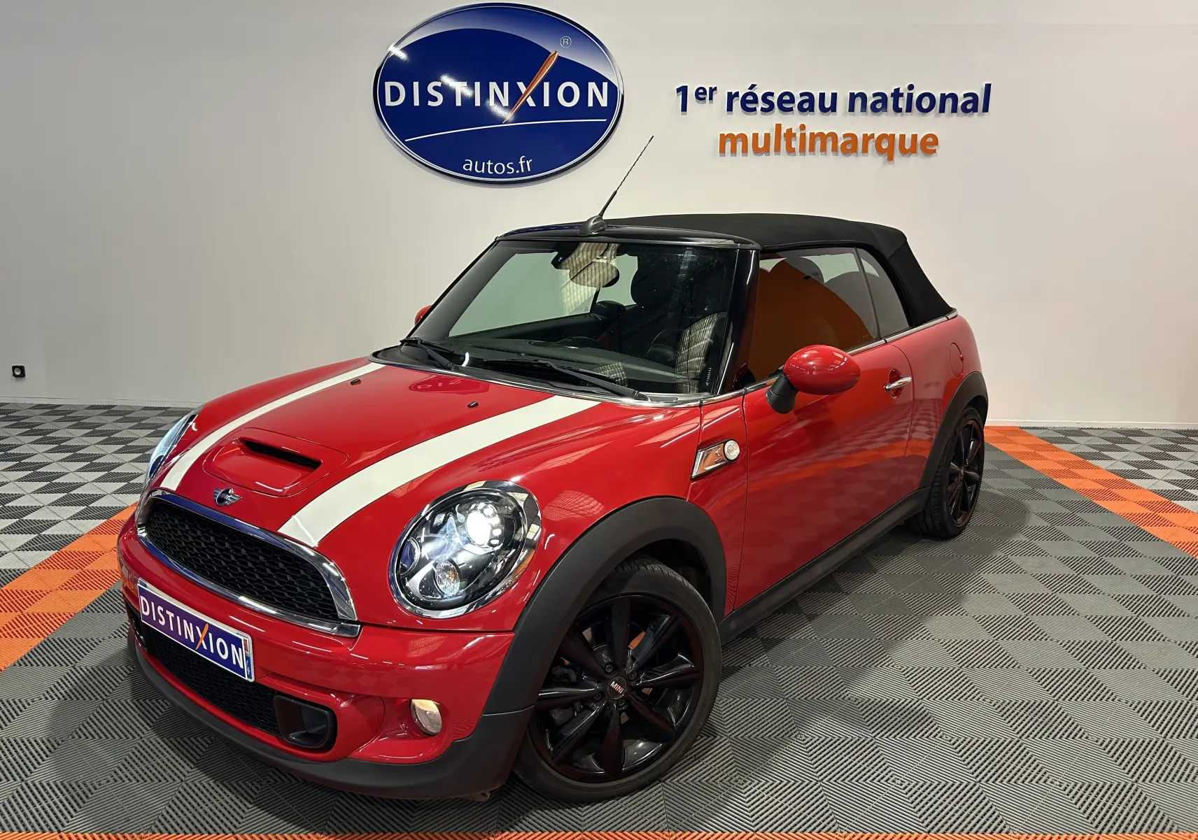 Vue 3/4 avant d'une MINI Cabriolet Cooper S rouge avec capote noire et jantes noires dans un showroom.