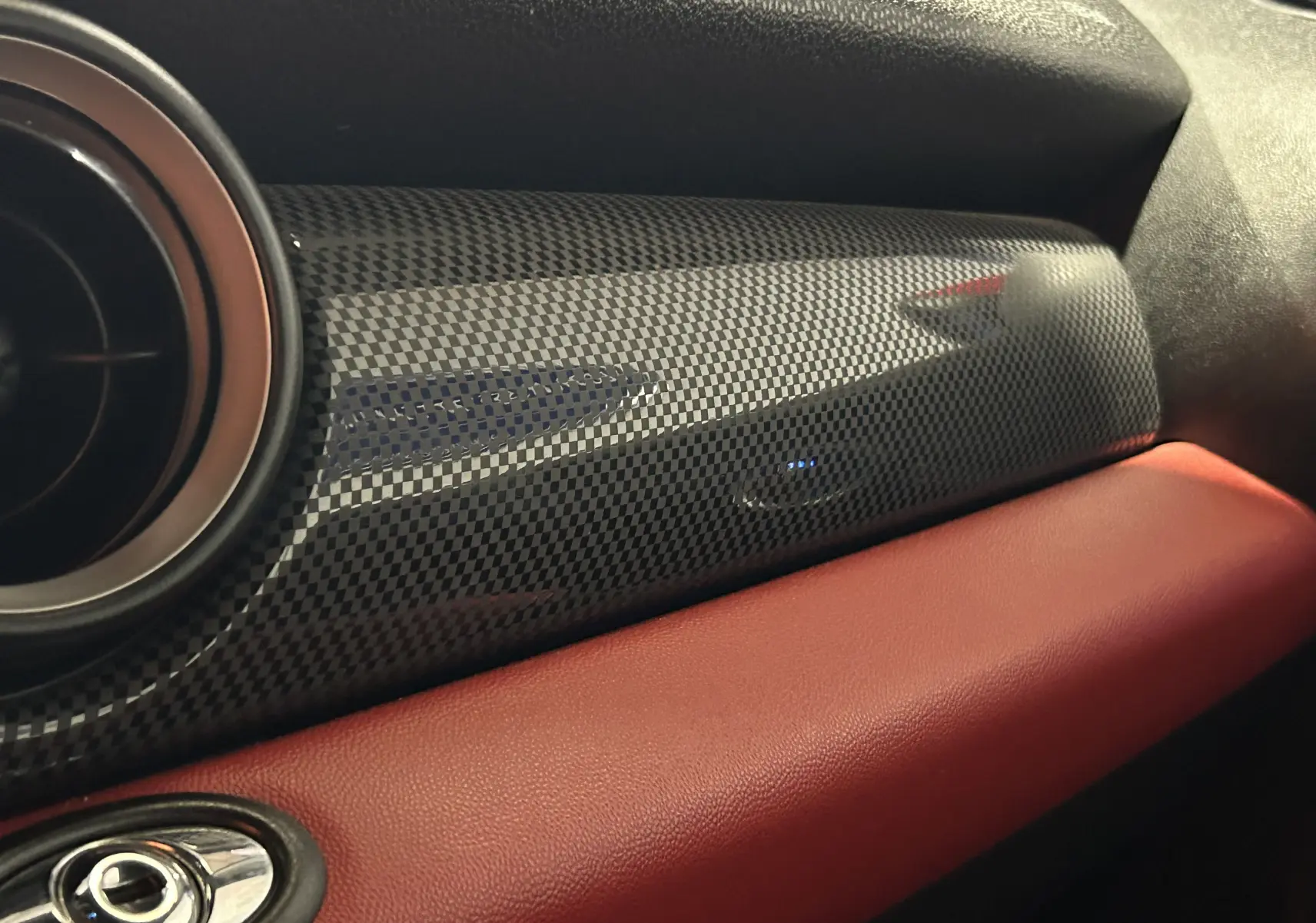 Gros plan sur la sortie d'air et le bouton de warning noir du tableau de bord d'une MINI Cabriolet rouge.