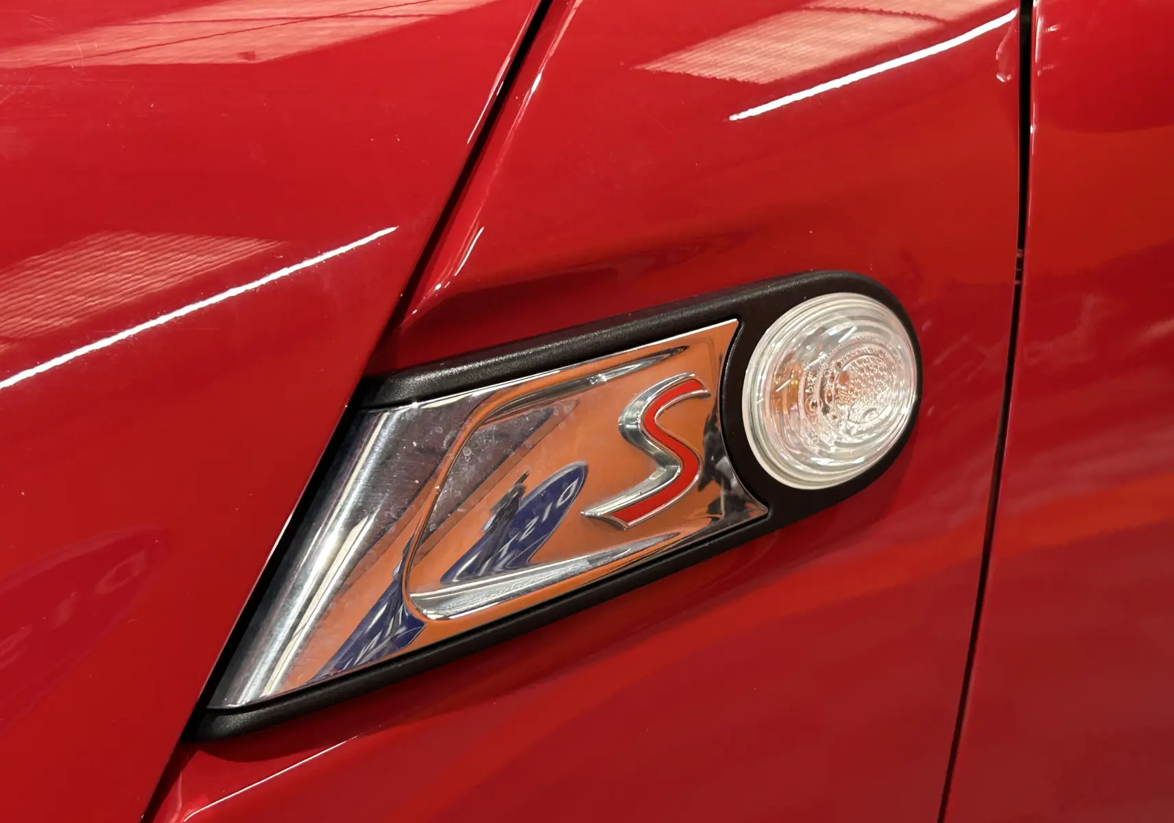 Gros plan sur l'emblème "S" chromé et le clignotant latéral sur la carrosserie rouge vif d'une MINI Cabriolet Cooper S.