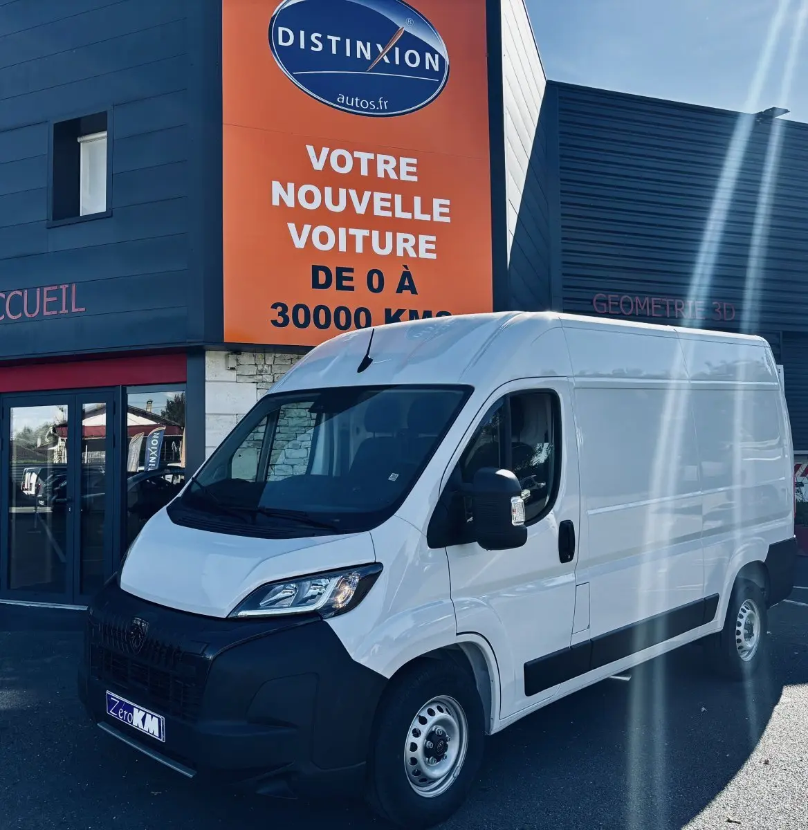 PEUGEOT Boxer Fourgon blanc vu en 3/4 avant droit devant un bâtiment commercial avec panneau orange.
