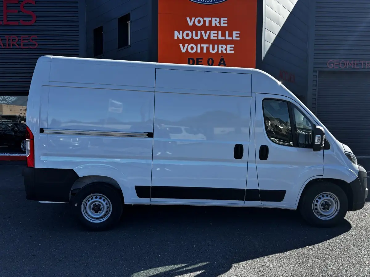 Profil côté gauche d’un fourgon Peugeot Boxer blanc L2H2 2025 avec porte coulissante et protections noires basses.