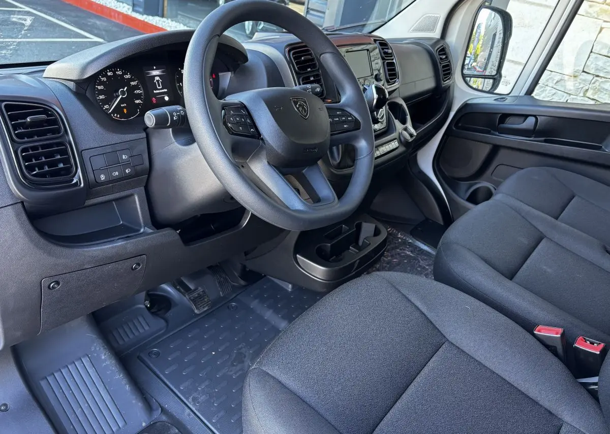 Intérieur du Peugeot Boxer Fourgon 2025 vu côté conducteur, tableau de bord noir avec volant multifonction et sièges gris.