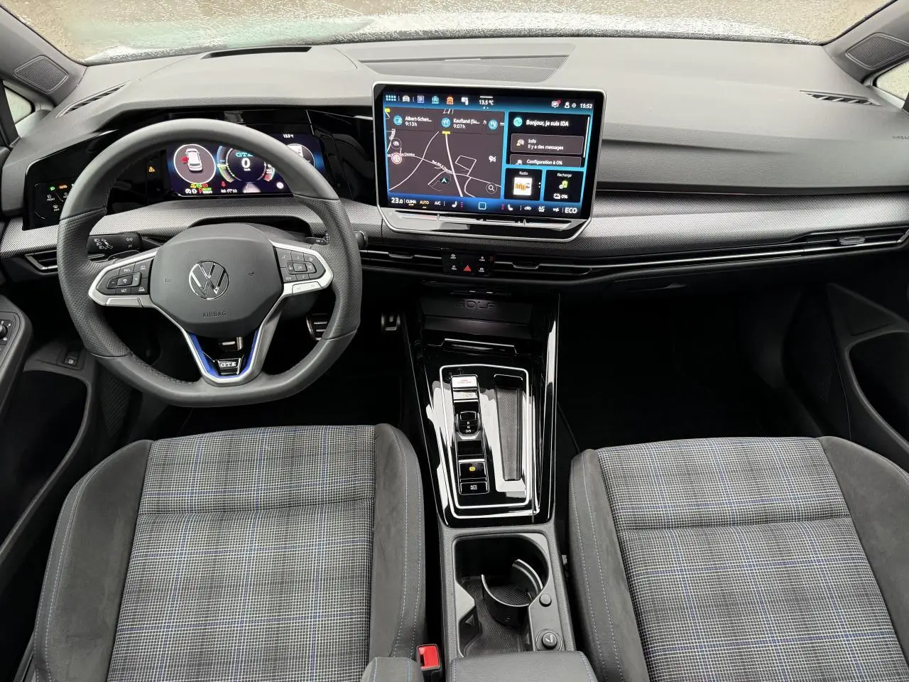 Vue intérieure avant de la Volkswagen Golf 1.5 eHybrid 2025, montrant le volant multifonctions, l’écran tactile central et les sièges sport à motif écossais.