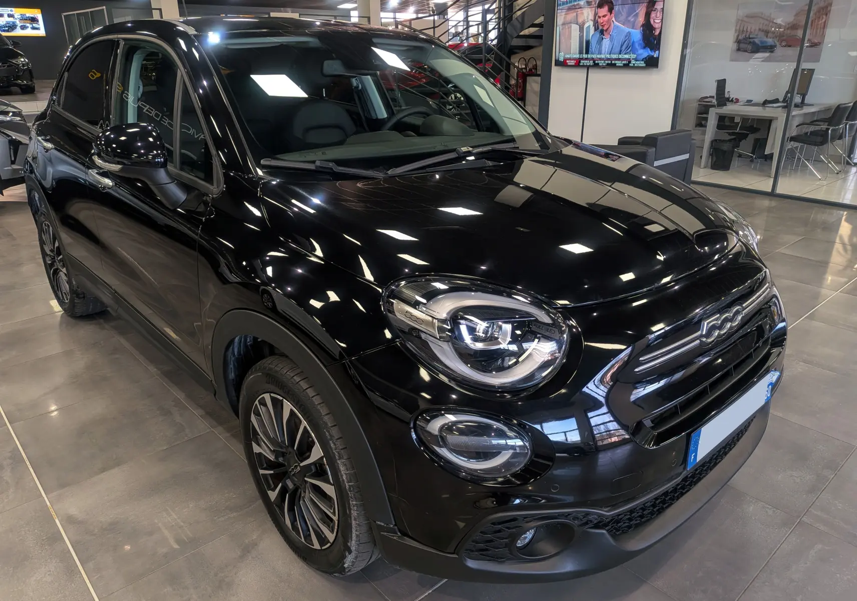 Fiat 500X noir cinéma vue 3/4 avant droit en showroom, mettant en valeur ses phares LED et jantes bi-ton.