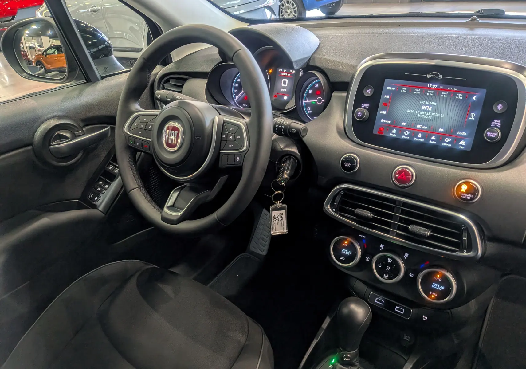 Vue intérieure côté conducteur de la Fiat 500X 2024 noire, avec tableau de bord numérique et écran tactile central allumé.