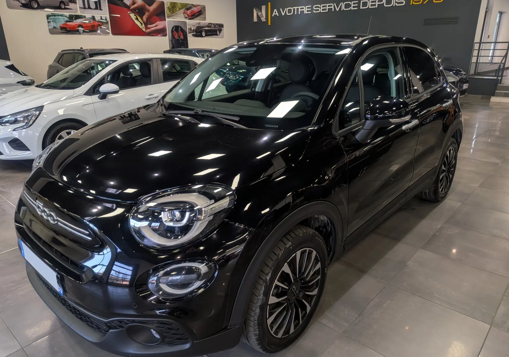 Vue 3/4 avant droite d'une FIAT 500X 2024 noir cinéma, avec jantes alliage et phares LED en showroom.
