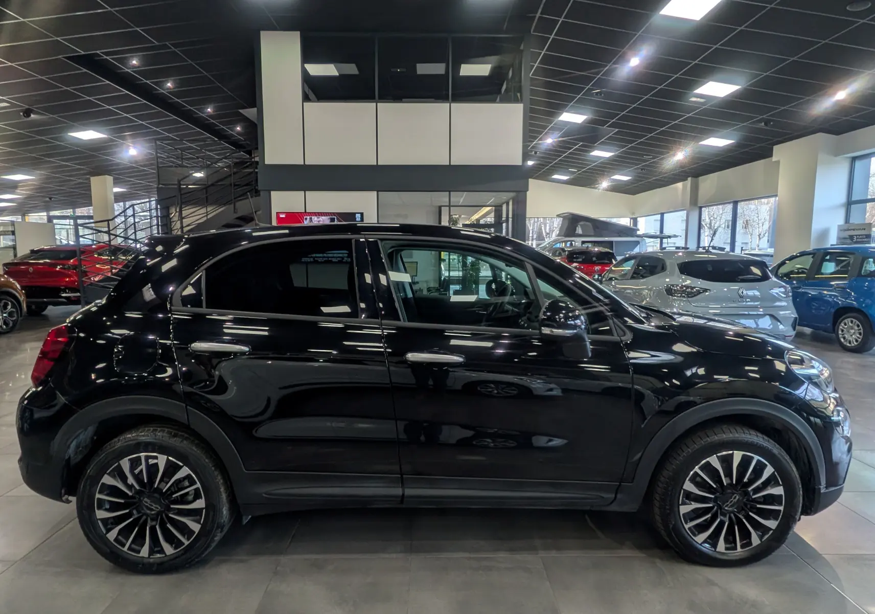 Vue de profil côté gauche d'une FIAT 500X noire Cinéma 2024 avec jantes alliage bicolores en showroom.