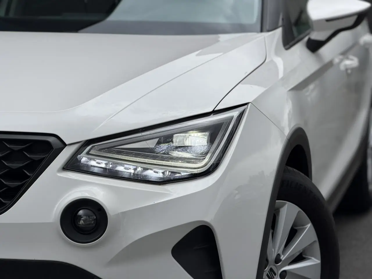 Gros plan sur l'avant droit blanc du SEAT Arona 2025, mettant en valeur le phare LED et le détecteur d'angles morts.
