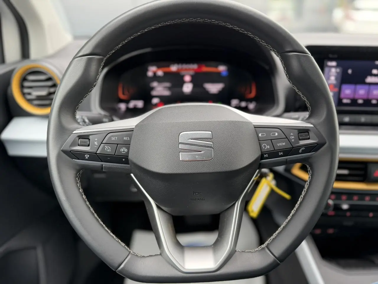 Vue rapprochée du volant noir de la SEAT Arona TSI 115 DSG Style avec commandes intégrées et tableau de bord digital flou.