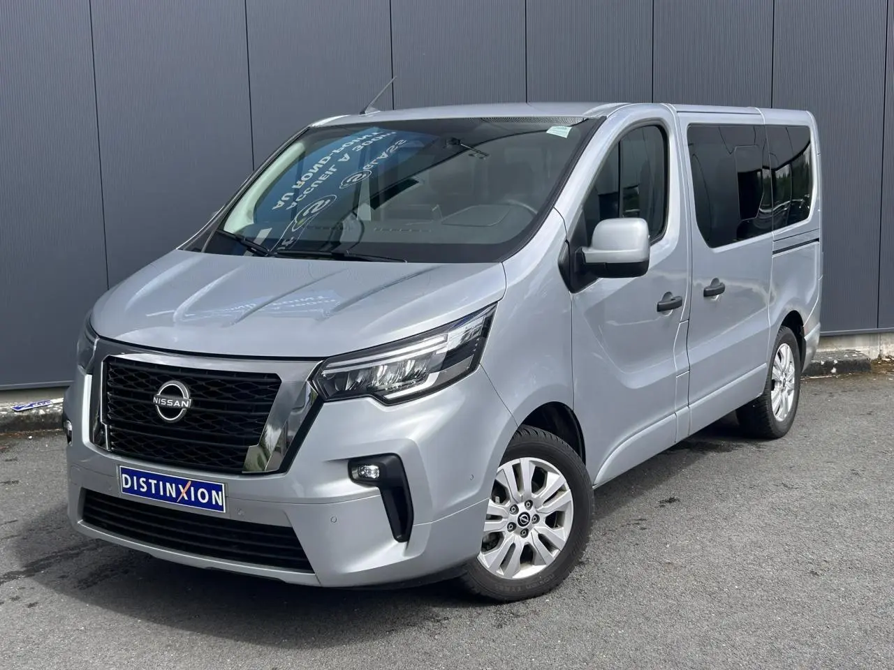 Nissan Primastar gris Highland vue 3/4 avant droit, hayon arrière vitré et vitres arrière surteintées visibles.