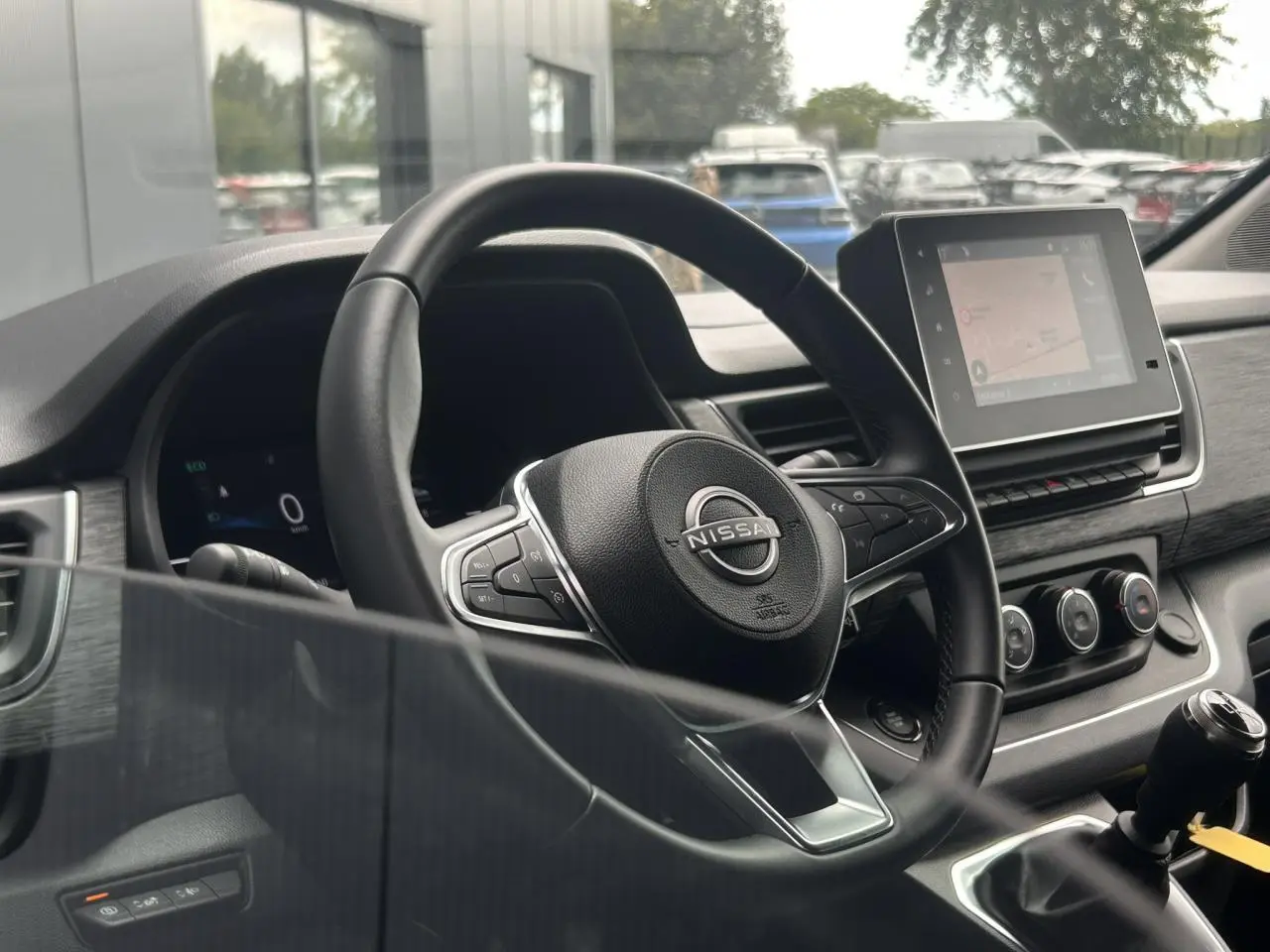 Vue intérieure centrée sur le volant Nissan et l'écran tactile du tableau de bord du Primastar gris Highland.
