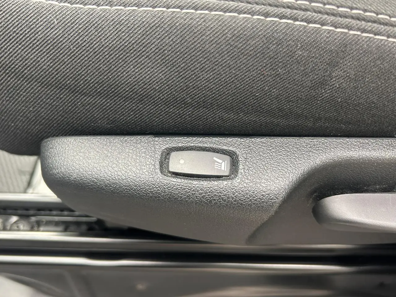 Gros plan sur le bouton de siège chauffant noir intégré à la garniture intérieure d’un Nissan Primastar gris Highland.