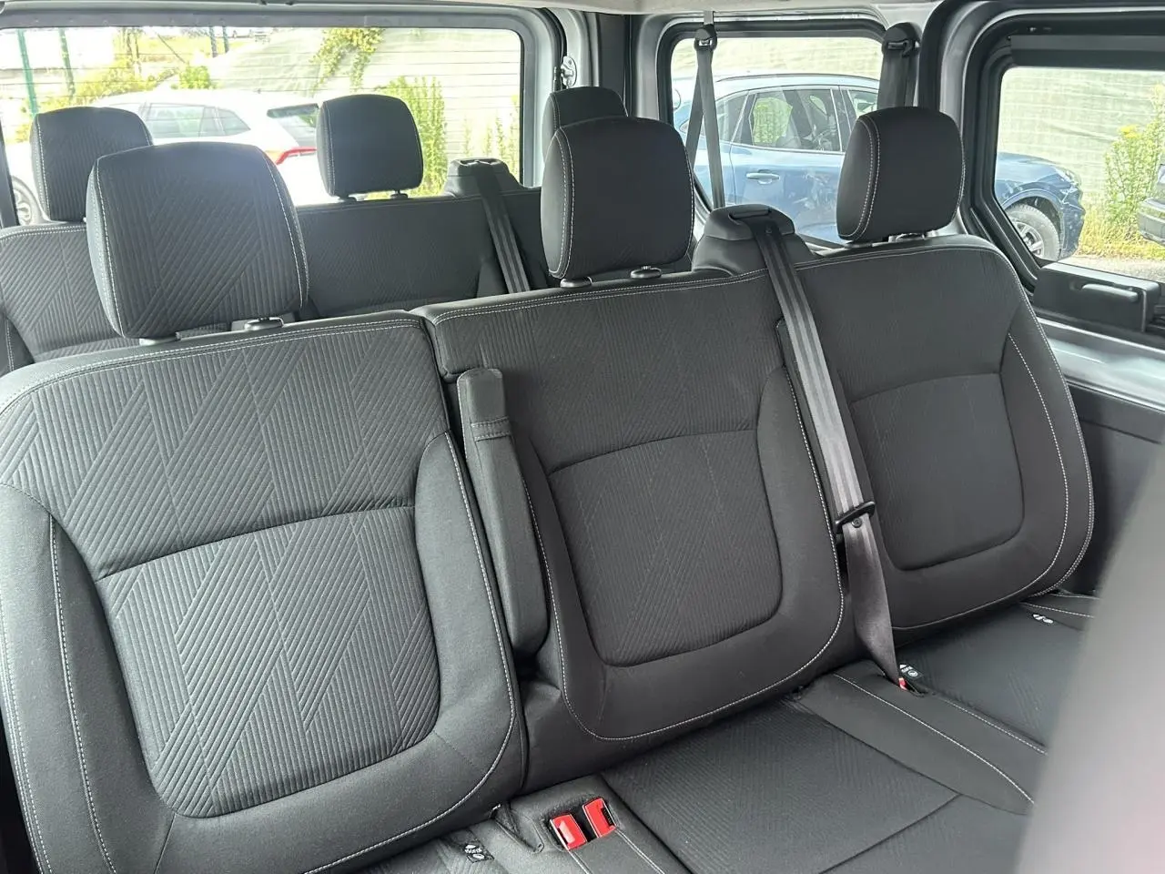 Vue intérieure sur les sièges arrière noirs du Nissan Primastar L1 3T 2.0 DCI 150 Tekna avec ceintures et appuie-têtes visibles.