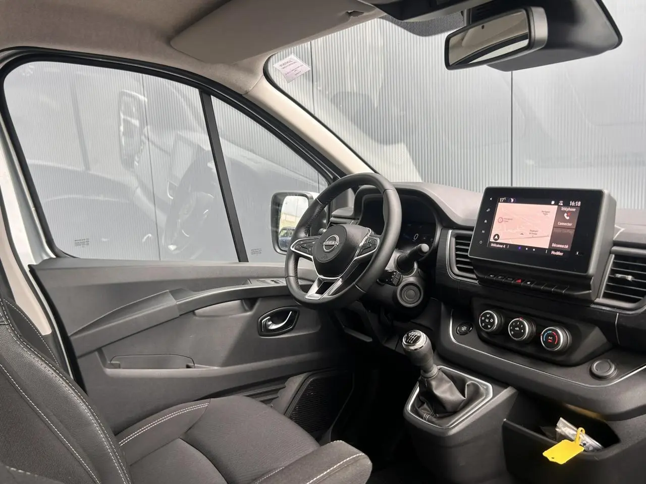 Vue intérieure côté conducteur du Nissan Primastar 2025 avec tableau de bord noir et écran tactile central.