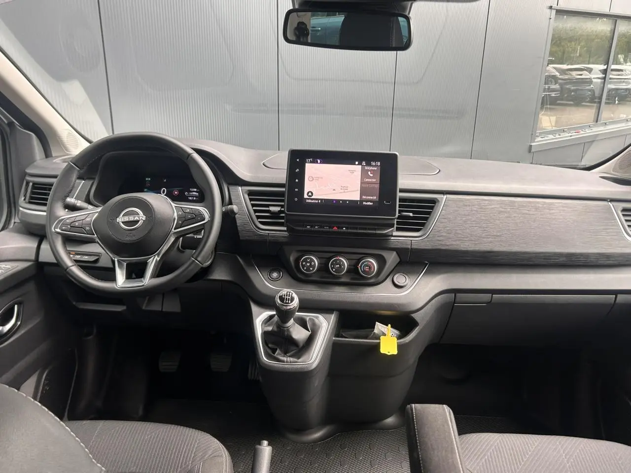 Vue intérieure frontale du tableau de bord du Nissan Primastar gris avec volant multifonction et écran tactile central.