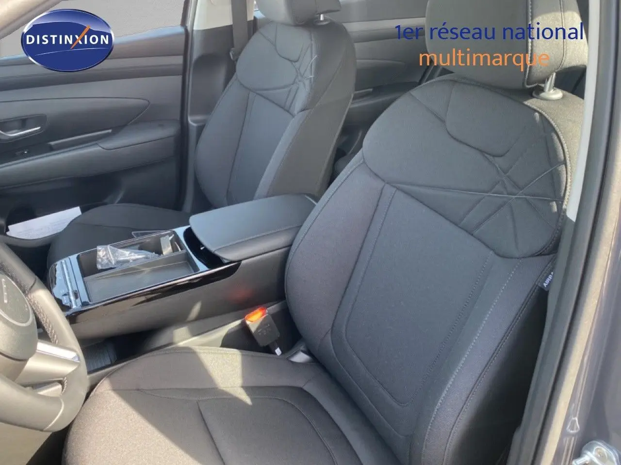 Vue intérieure rapprochée des sièges avant en tissu noir du Hyundai Tucson 2026 avec accoudoir central et console brillante.