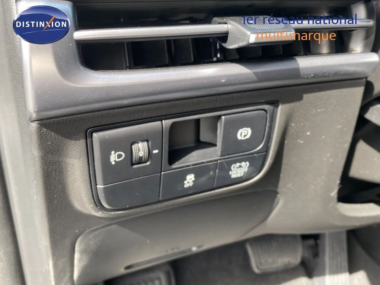 Détail des commandes côté gauche sous la ventilation du Hyundai Tucson gris Ecotronic 2026, avec boutons d'éclairage et frein à main électronique.