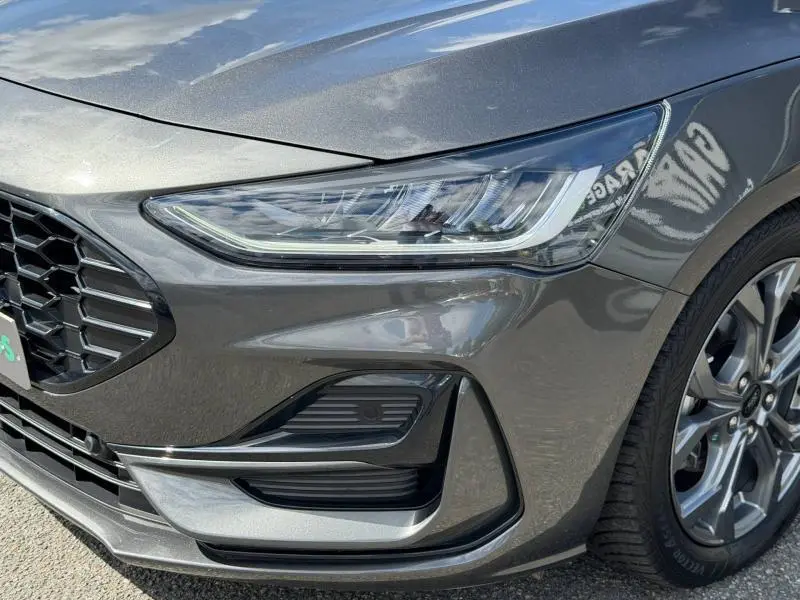 Gros plan sur l'avant droit gris lunaire métallisé de la Ford Focus 2025, mettant en valeur le phare LED et la calandre noire.