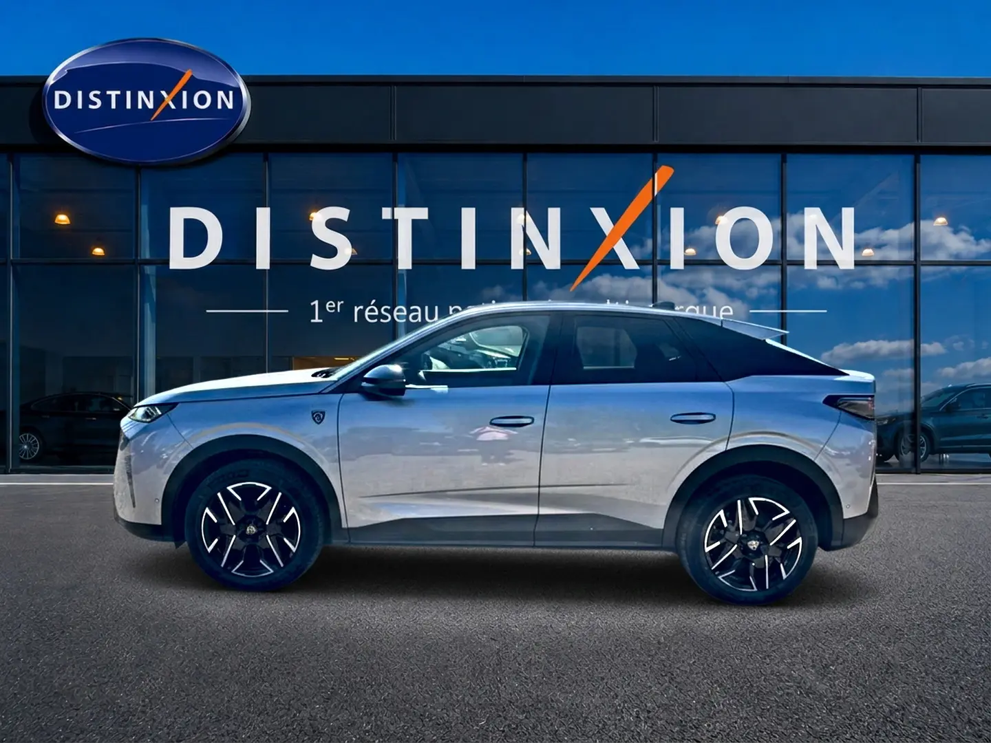 Vue de profil côté gauche d'un Peugeot 3008 gris 2025 garé devant une vitrine avec logo Distinxion.