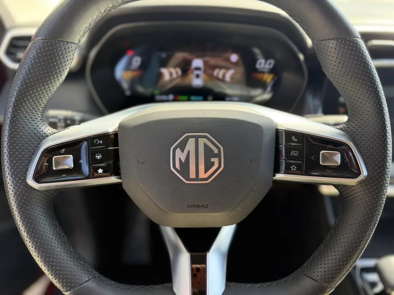Vue rapprochée du volant en cuir noir perforé avec logo MG au centre, tableau de bord numérique en arrière-plan flou.