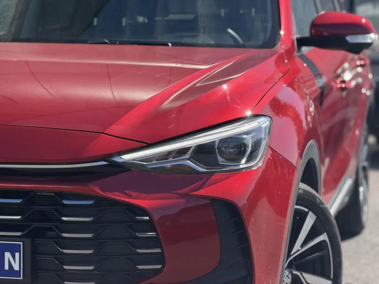 Gros plan sur l'avant droit rouge Diamond du MG ZS 1.5 Hybrid+ 197 Luxury, mettant en valeur le phare LED et la calandre noire.