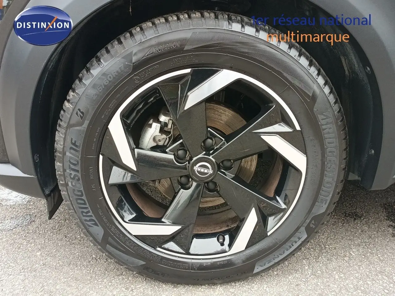 Gros plan sur la roue avant droite noire métallisée du Nissan Juke Hybrid 2024 avec jante alliage bicolore.