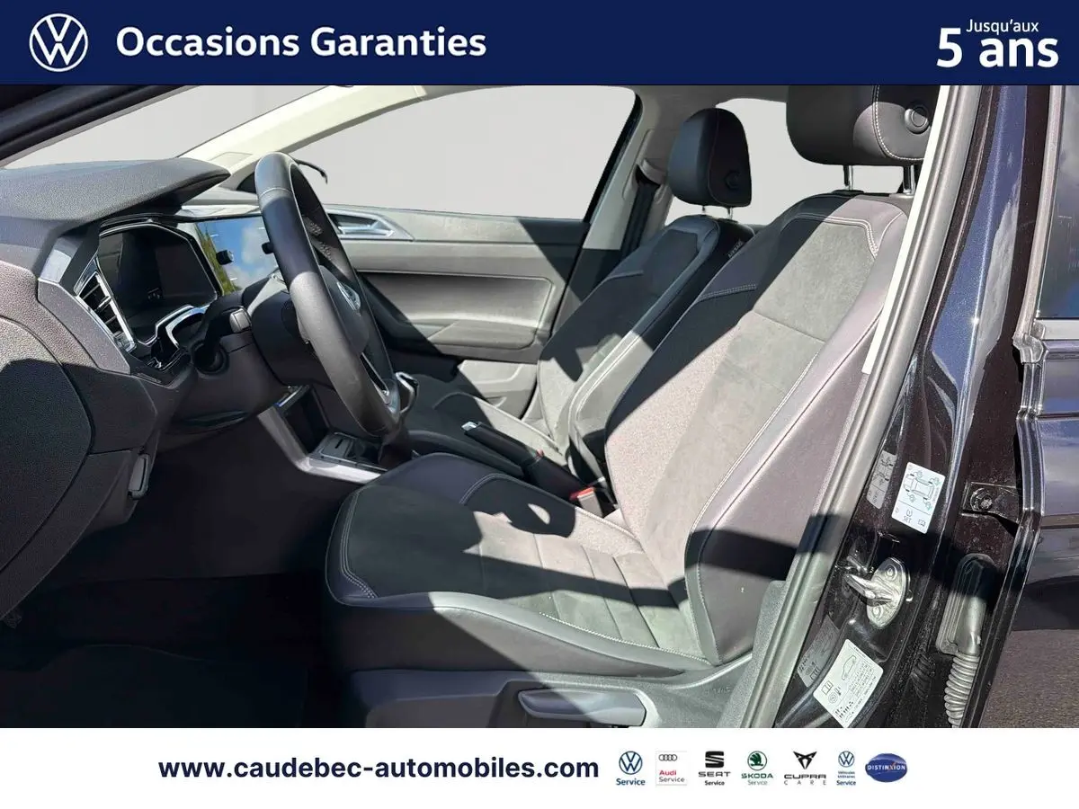 Vue intérieure côté conducteur de la Volkswagen Polo noire intense nacrée, montrant sièges et tableau de bord modernes.