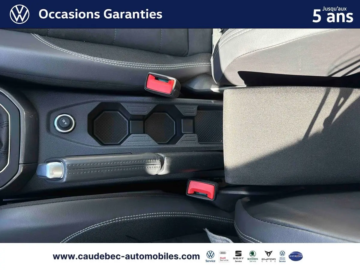 Vue plongeante sur la console centrale et frein à main d’une Volkswagen Polo noire avec sellerie cuir noire et surpiqûres blanches.