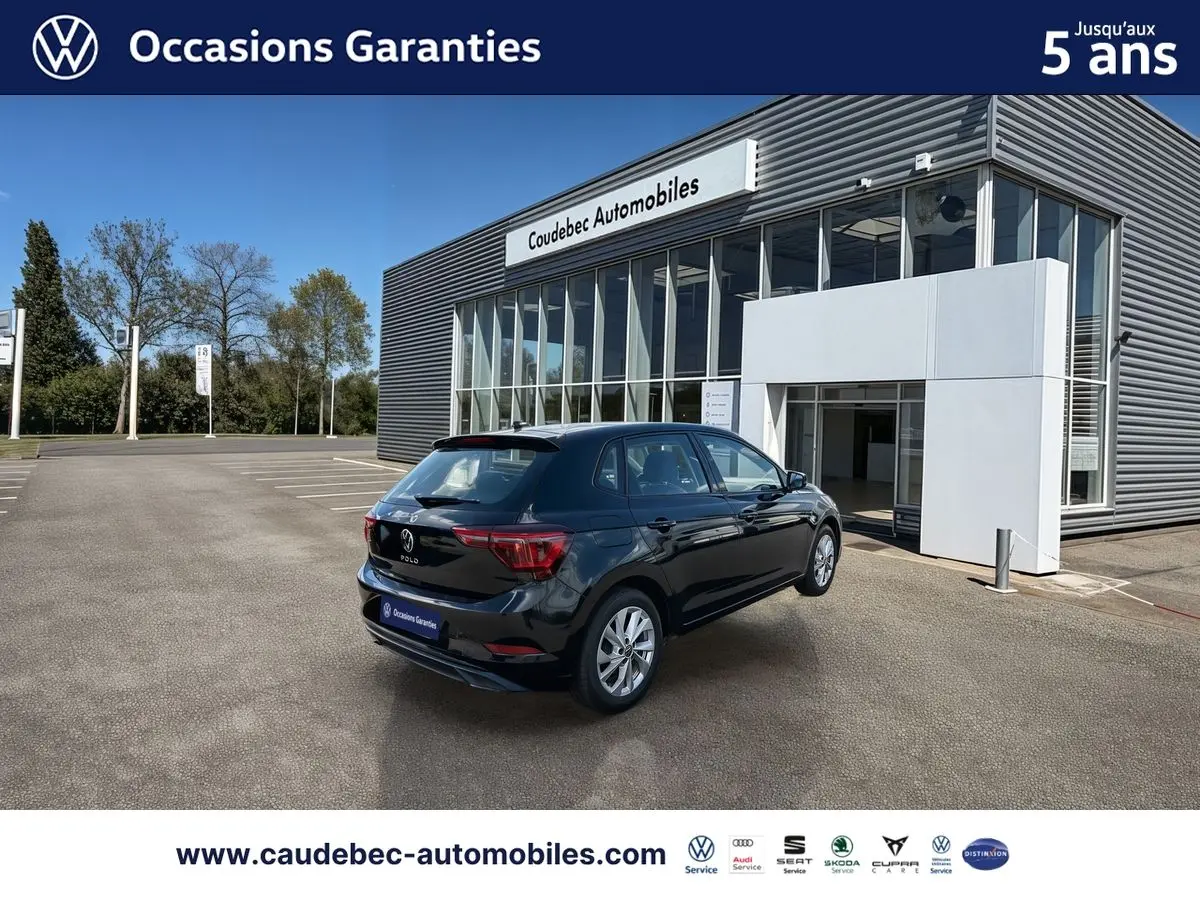 Volkswagen Polo noir intense nacré vue 3/4 arrière droit devant un bâtiment de concession Caudebec Automobiles.