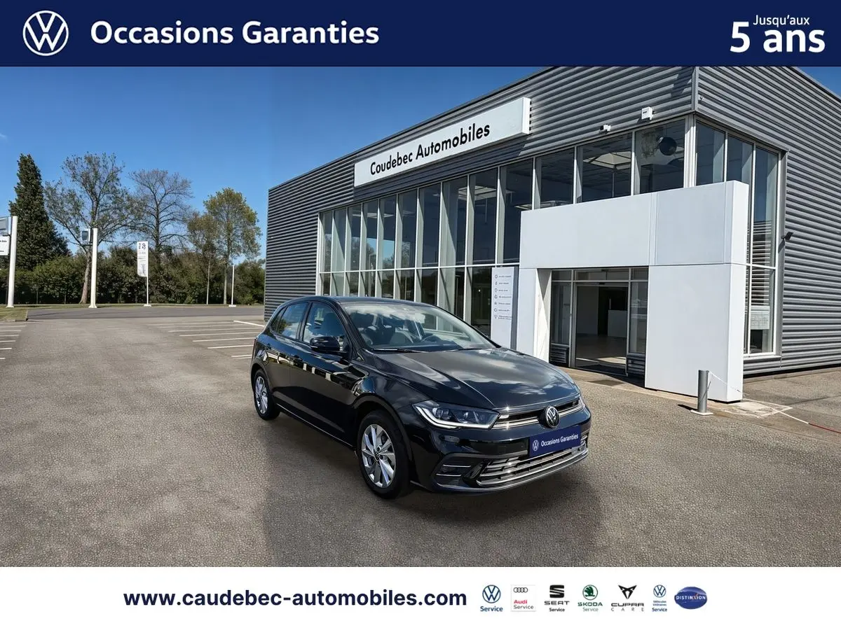 Volkswagen Polo noir intense nacré vue 3/4 avant droit, garée devant un bâtiment moderne de concession.