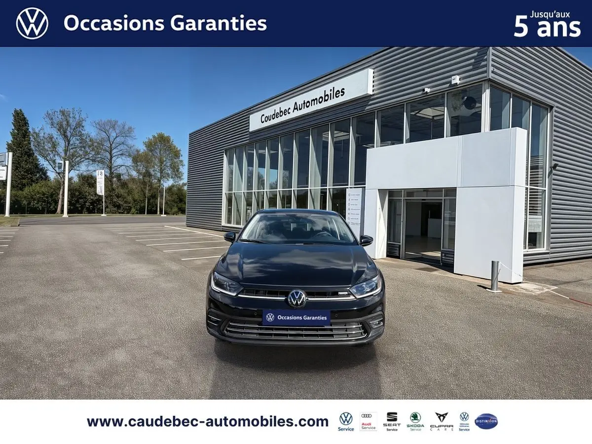 Volkswagen Polo noir intense nacré vue de face devant un bâtiment moderne de concession automobile.