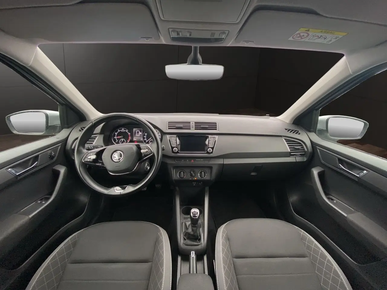 Vue intérieure frontale du tableau de bord et volant noir d'une Skoda Fabia gris argent, avec écran tactile et boîte manuelle.