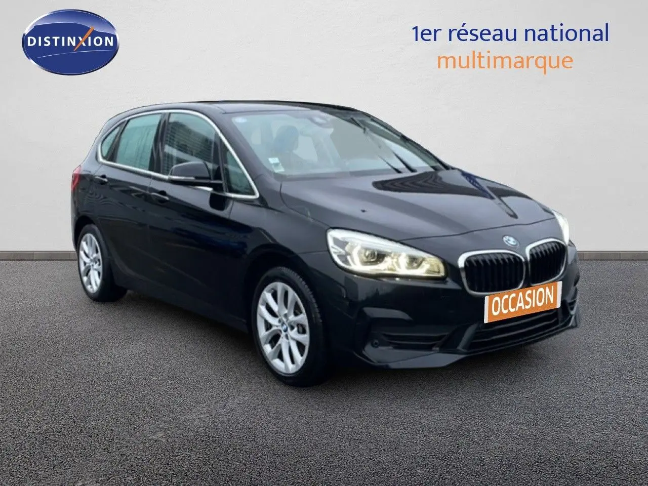 BMW Série 2 Active Tourer noir saphir métal, vue 3/4 avant droit avec phares allumés sur fond neutre.