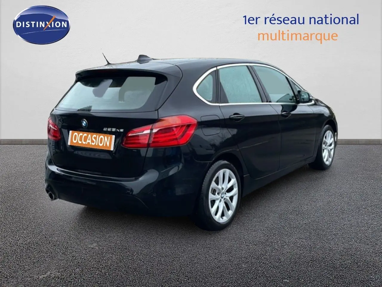 BMW Série 2 Active Tourer noir saphir métal vue 3/4 arrière droit sur sol gris, avec feux arrière allumés.