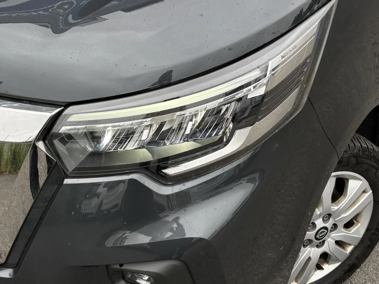 Gros plan sur le phare avant droit et la jante alliage 17'' du Nissan Primastar gris Comète, version 2025.