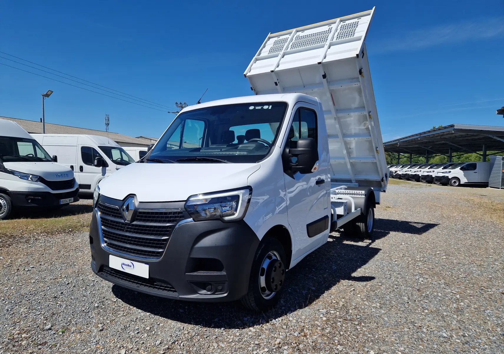 Vue 3/4 avant gauche d'un Renault Master blanc avec benne relevée et roues jumelées sur un terrain extérieur.