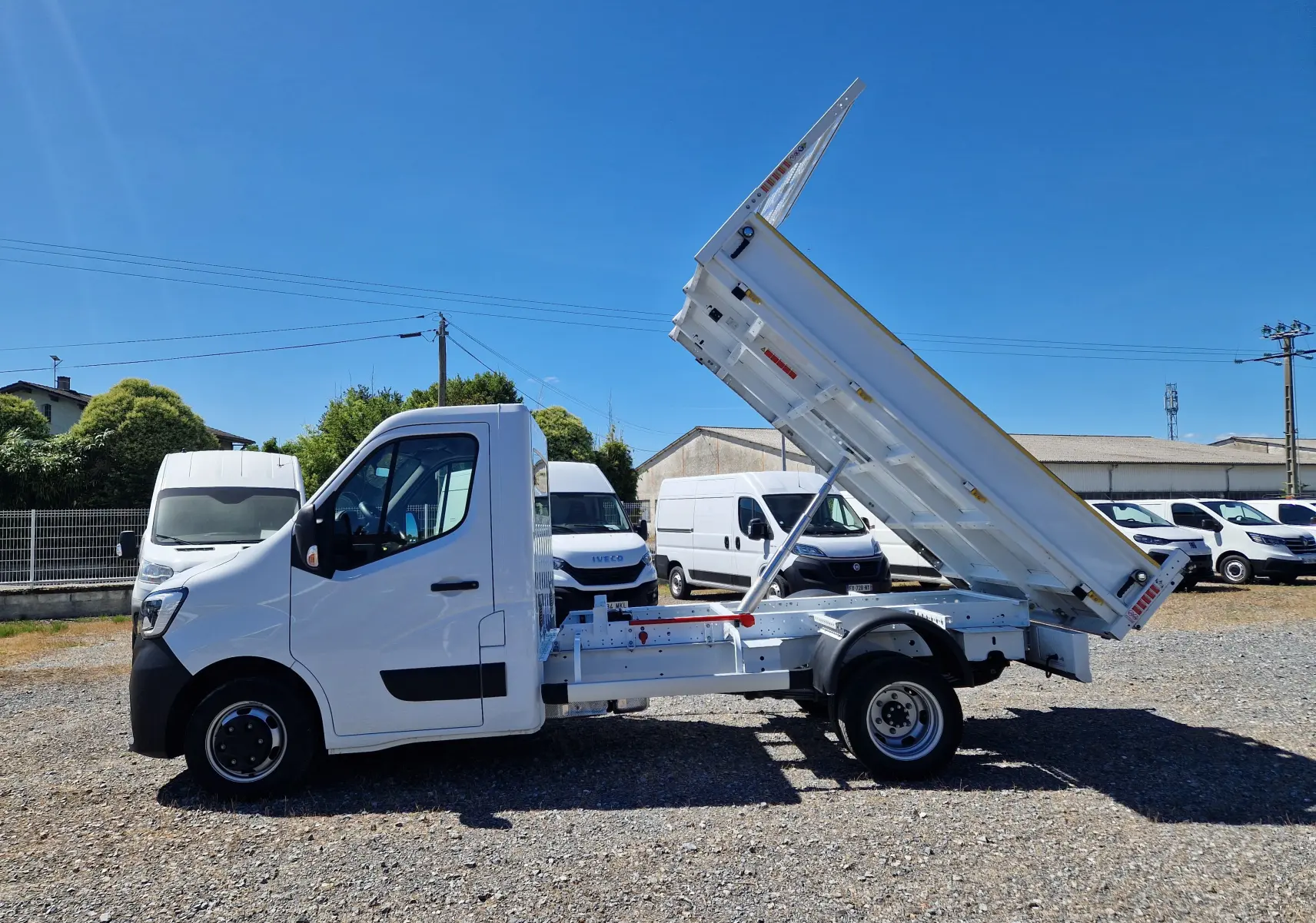 Vue de profil côté gauche du Renault Master blanc avec benne basculante relevée sur un terrain extérieur.
