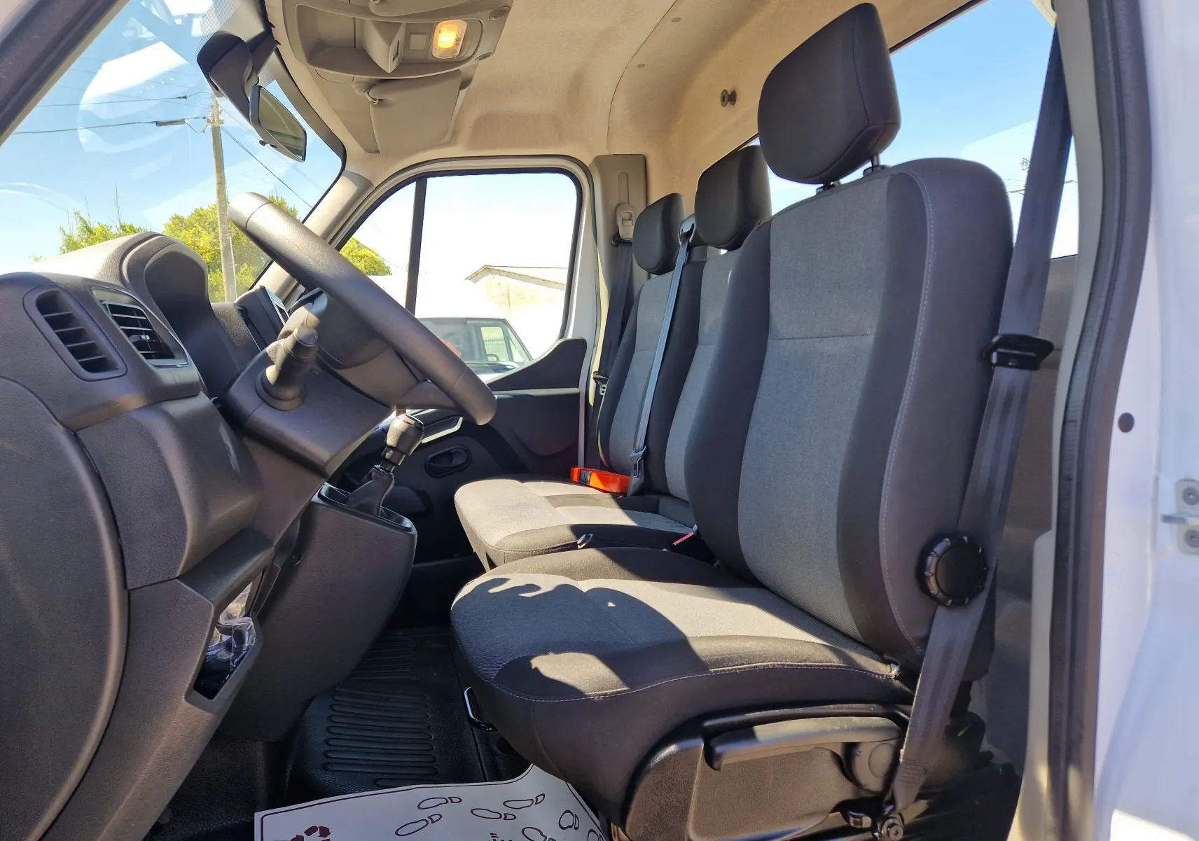 Vue intérieure côté conducteur du Renault Master Châssis Cabine blanc 2024, montrant les sièges tissu gris et noir et le volant.
