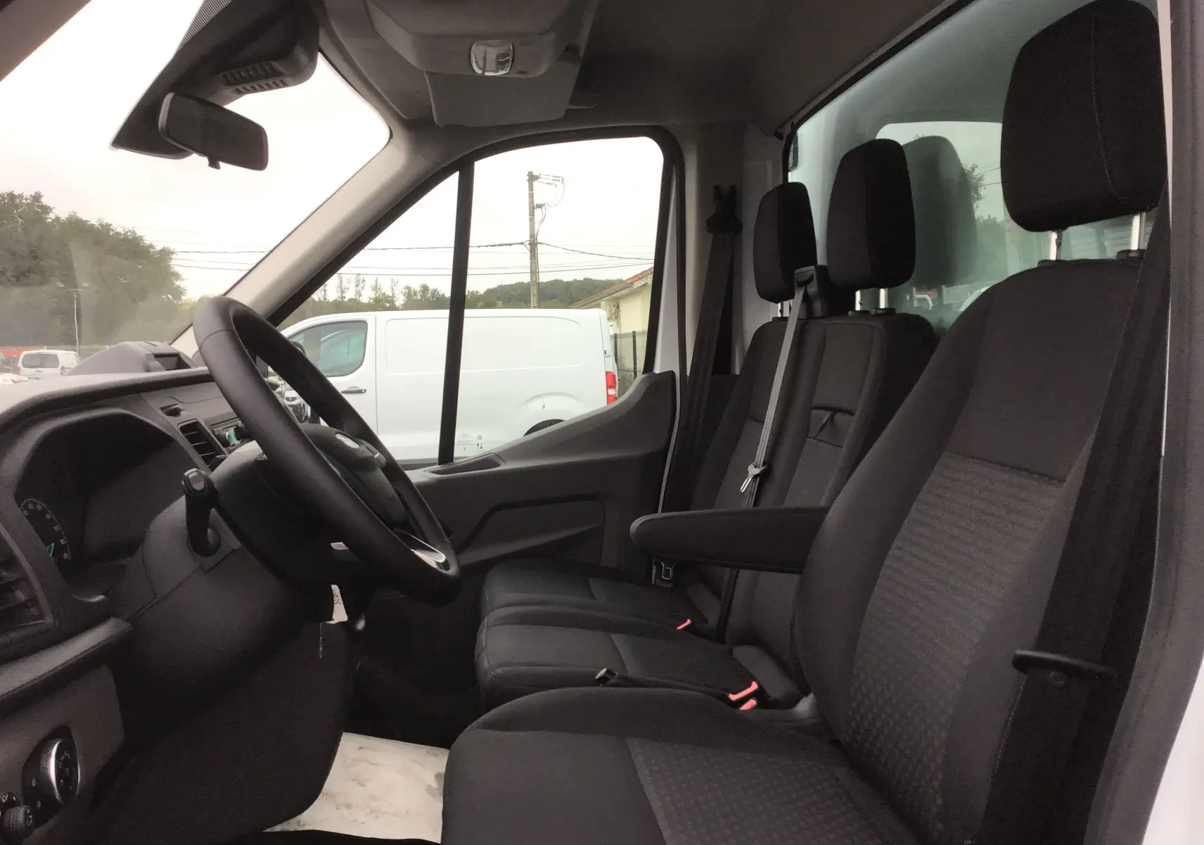 Vue intérieure côté conducteur du Ford Transit Chassis Cabine blanc 2024 avec sièges noirs et tableau de bord simple.