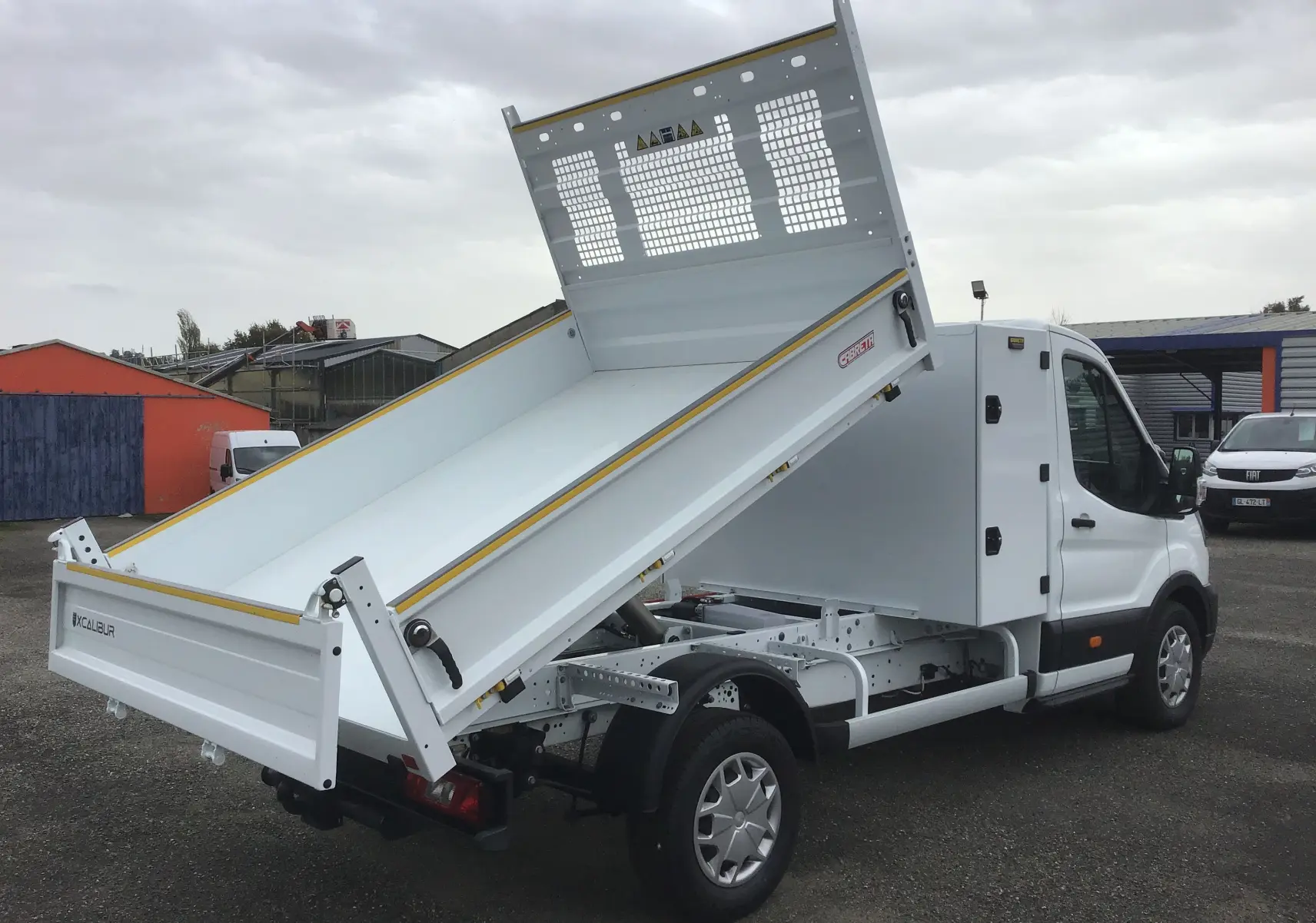 Ford Transit Chassis Cabine blanc vu en 3/4 arrière droit avec benne relevée et coffre acier visible.
