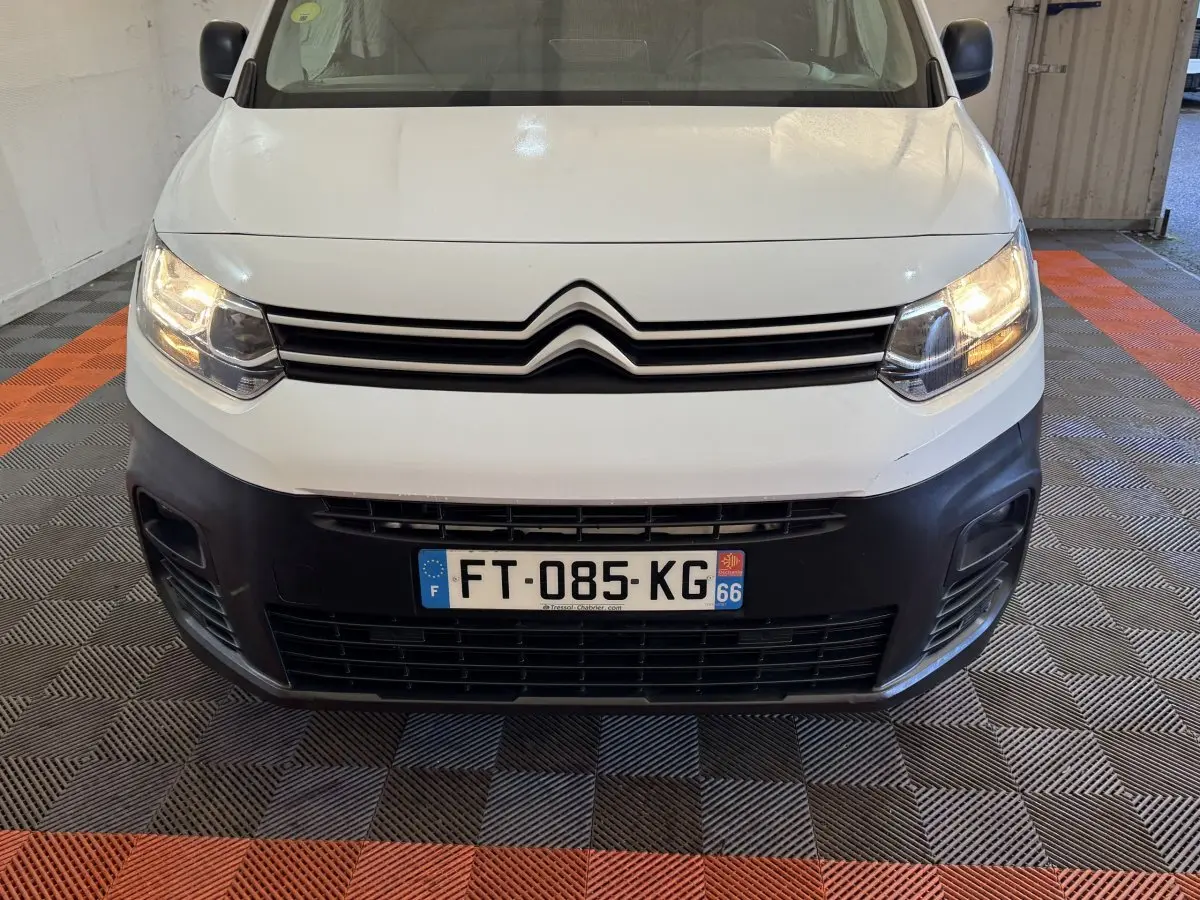 Vue avant d’un Citroën Berlingo blanc de 2020 avec phares allumés et pare-chocs noir dans un garage.