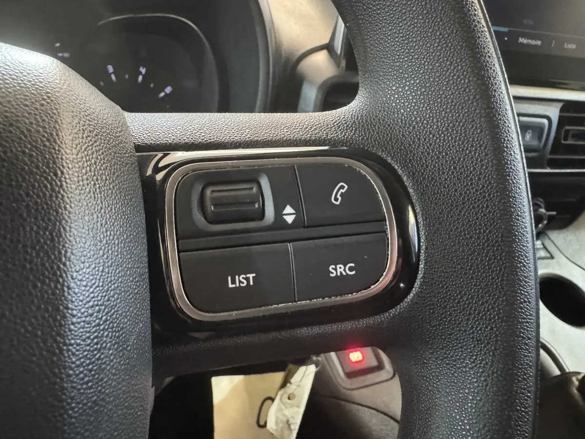 Gros plan sur les commandes multifonctions noires du volant d’un Citroën Berlingo blanc, intérieur côté conducteur.