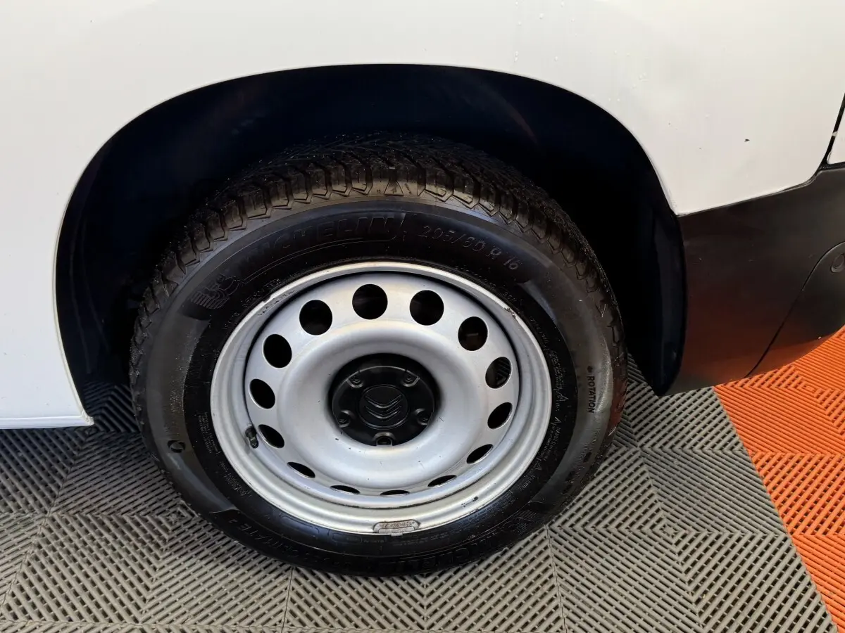 Gros plan sur la roue avant gauche en jante acier du Citroën Berlingo blanc, avec partie de la carrosserie visible.
